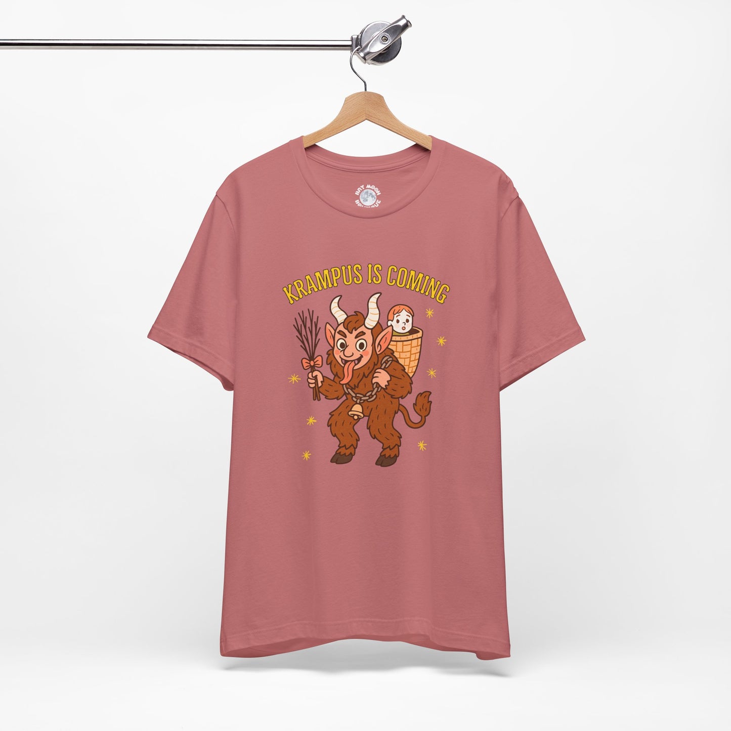 Pink t-shirt with cartoon character and text 'Kämpus is Coming' on a hanger against a white background