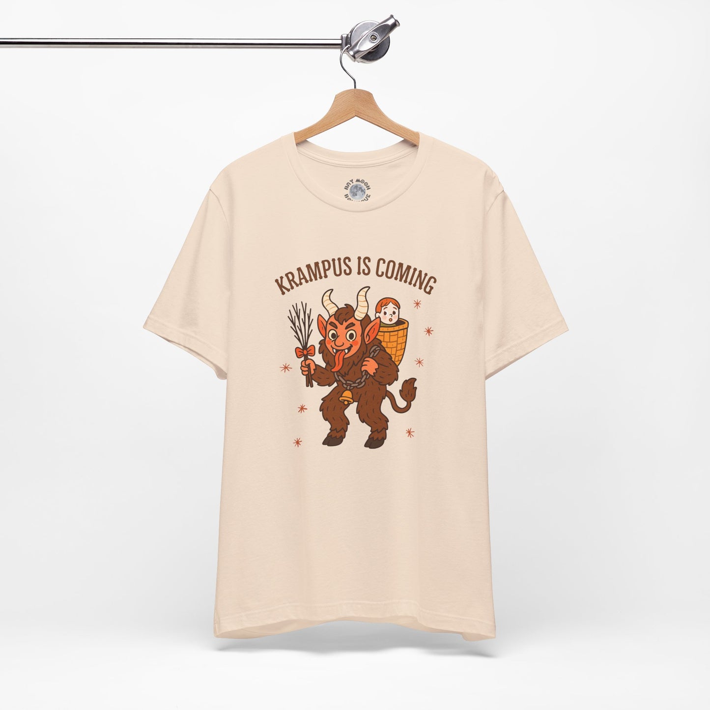 Beige t-shirt with Krampus graphic and text 'Krampus is Coming' on a hanger against a white background
