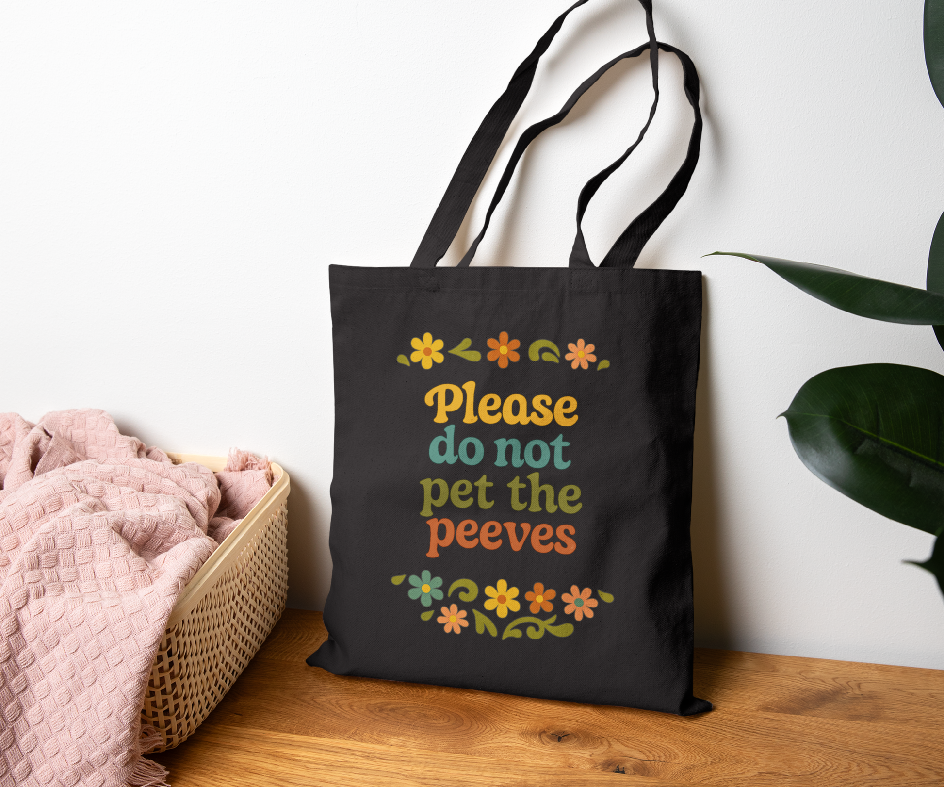 Black tote bag with colorful text please do not pet the peeves and floral designs on a wooden surface.