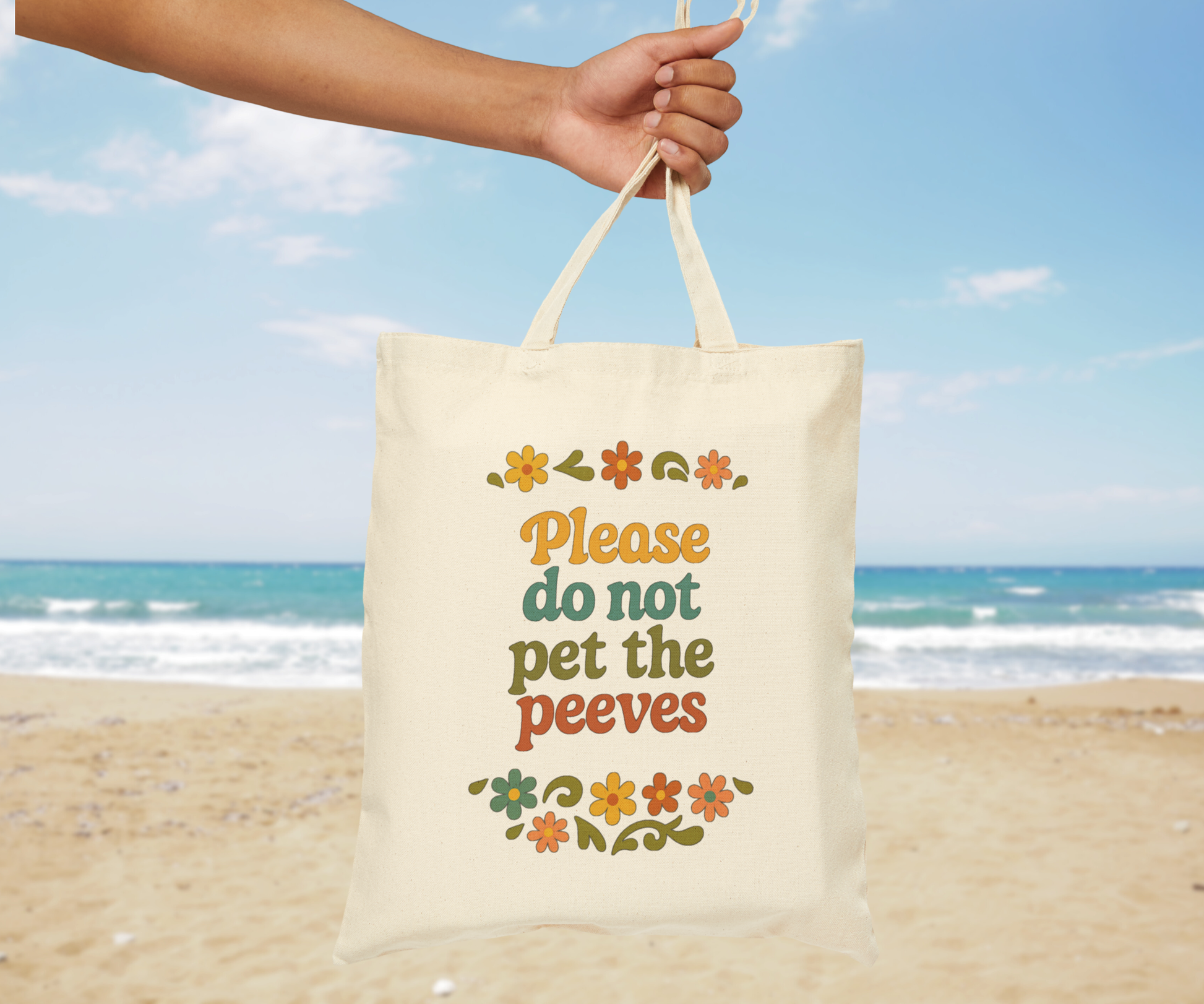 Tote bag with text 'Please do not pet the peeves' held by a hand on a beach.
