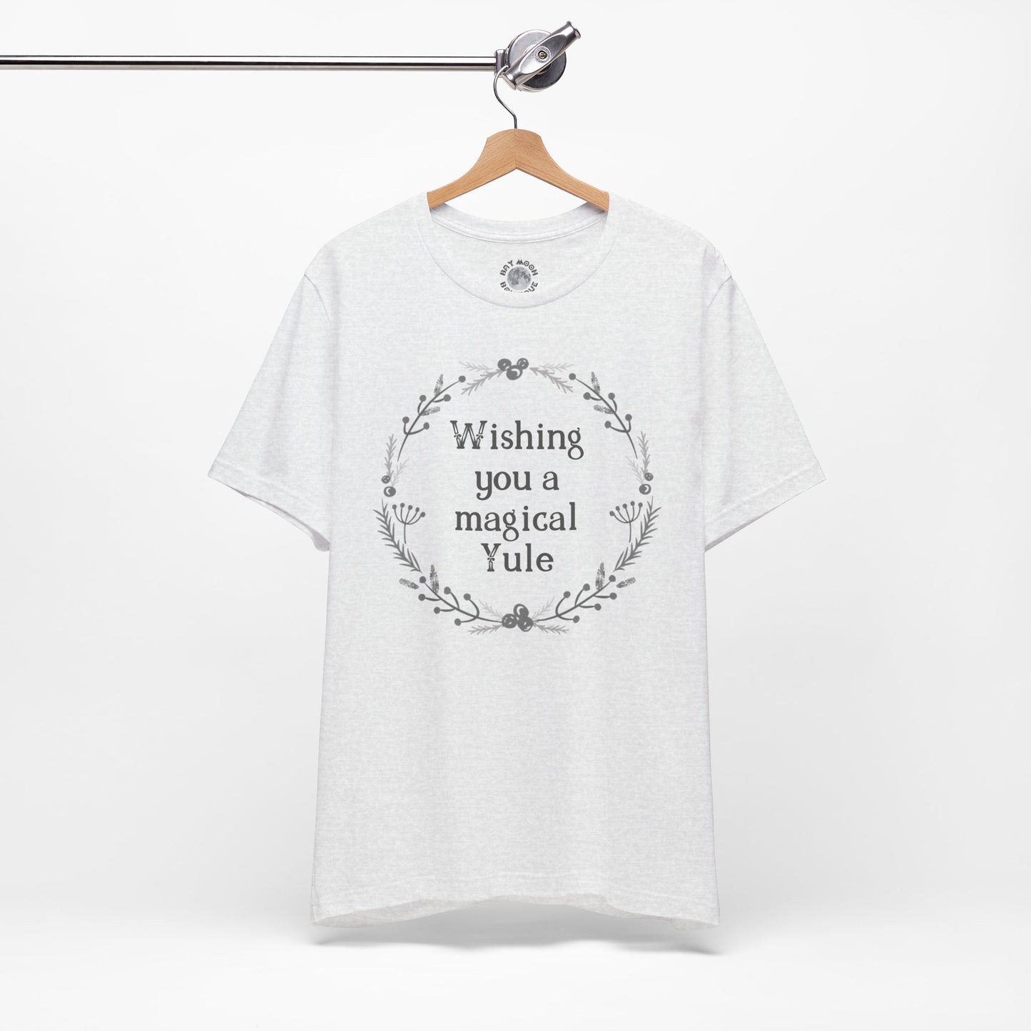 Ash gray t-shirt with 'Wishing you a magical Yule' text on a hanger against a white background