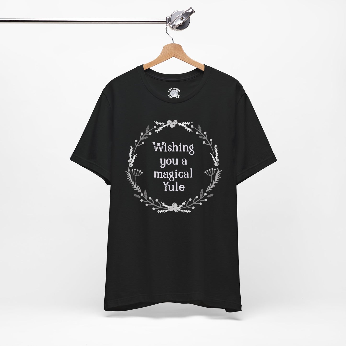 Black t-shirt with 'Wishing you a magical Yule' text on a hanger against a white background
