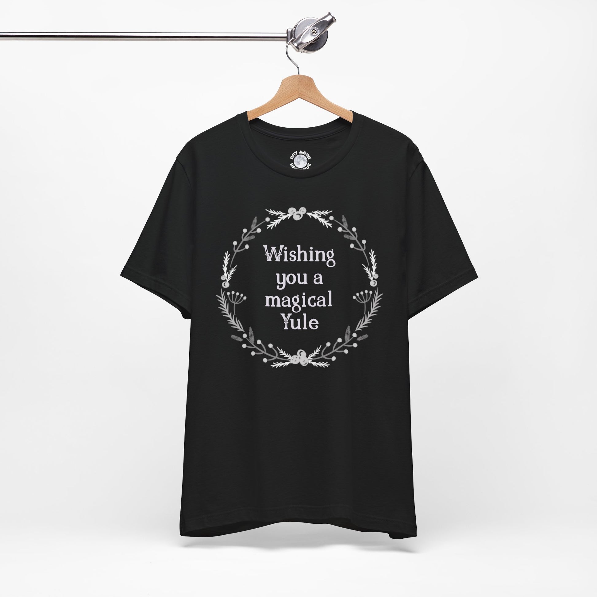 Black t-shirt with 'Wishing you a magical Yule' text on a hanger against a white background