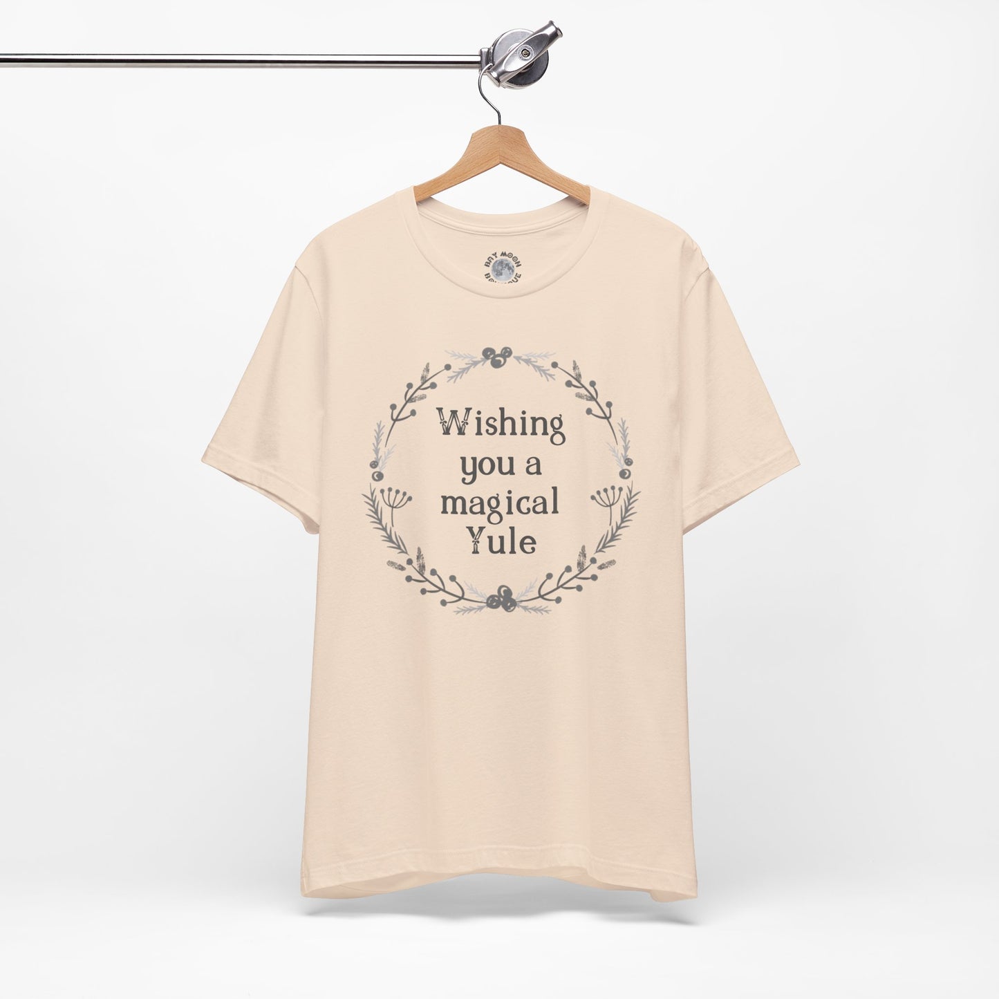 Beige t-shirt with 'Wishing you a magical Yule' text on a hanger against a white background
