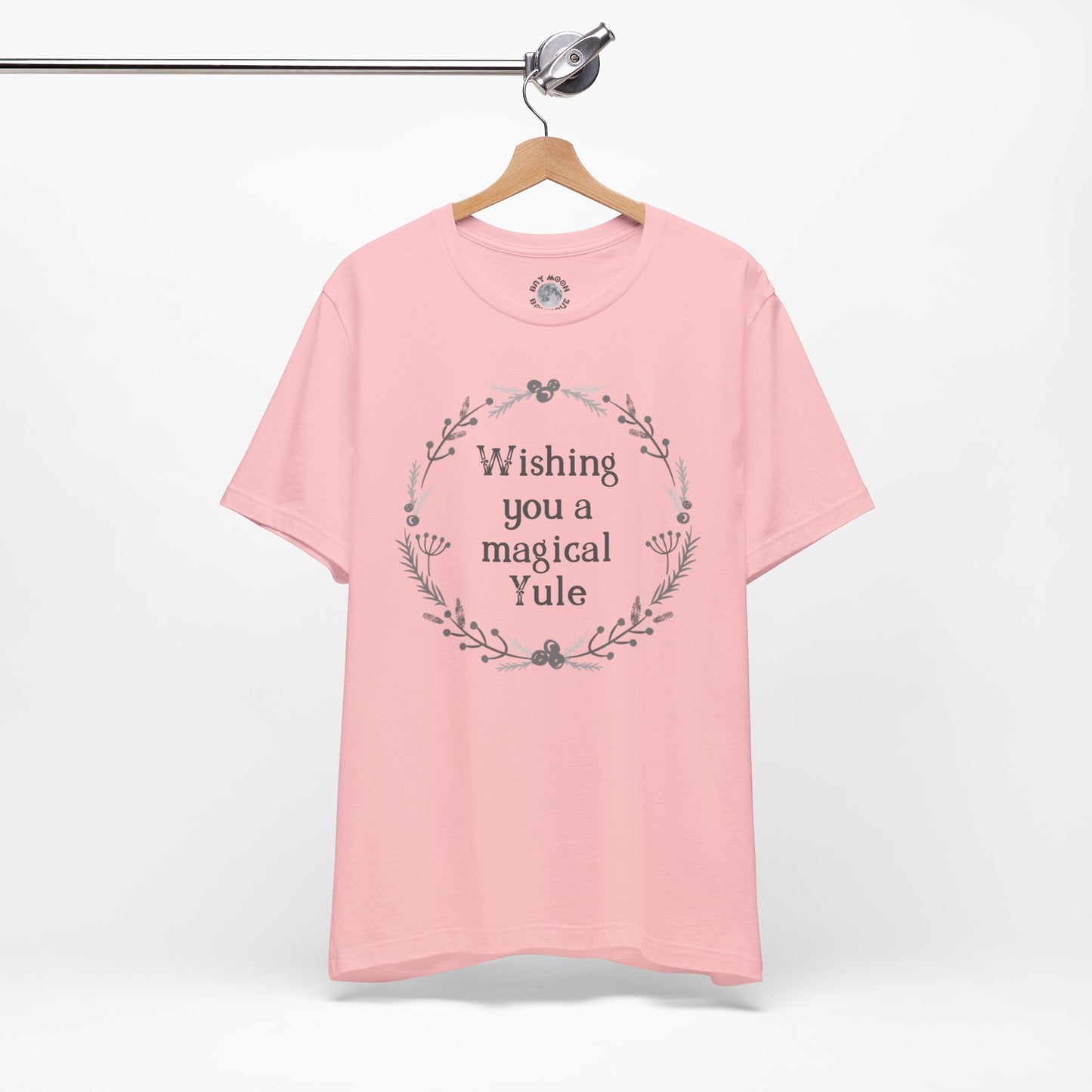 Pink t-shirt with 'Wishing you a magical Yule' text on a hanger against a white background